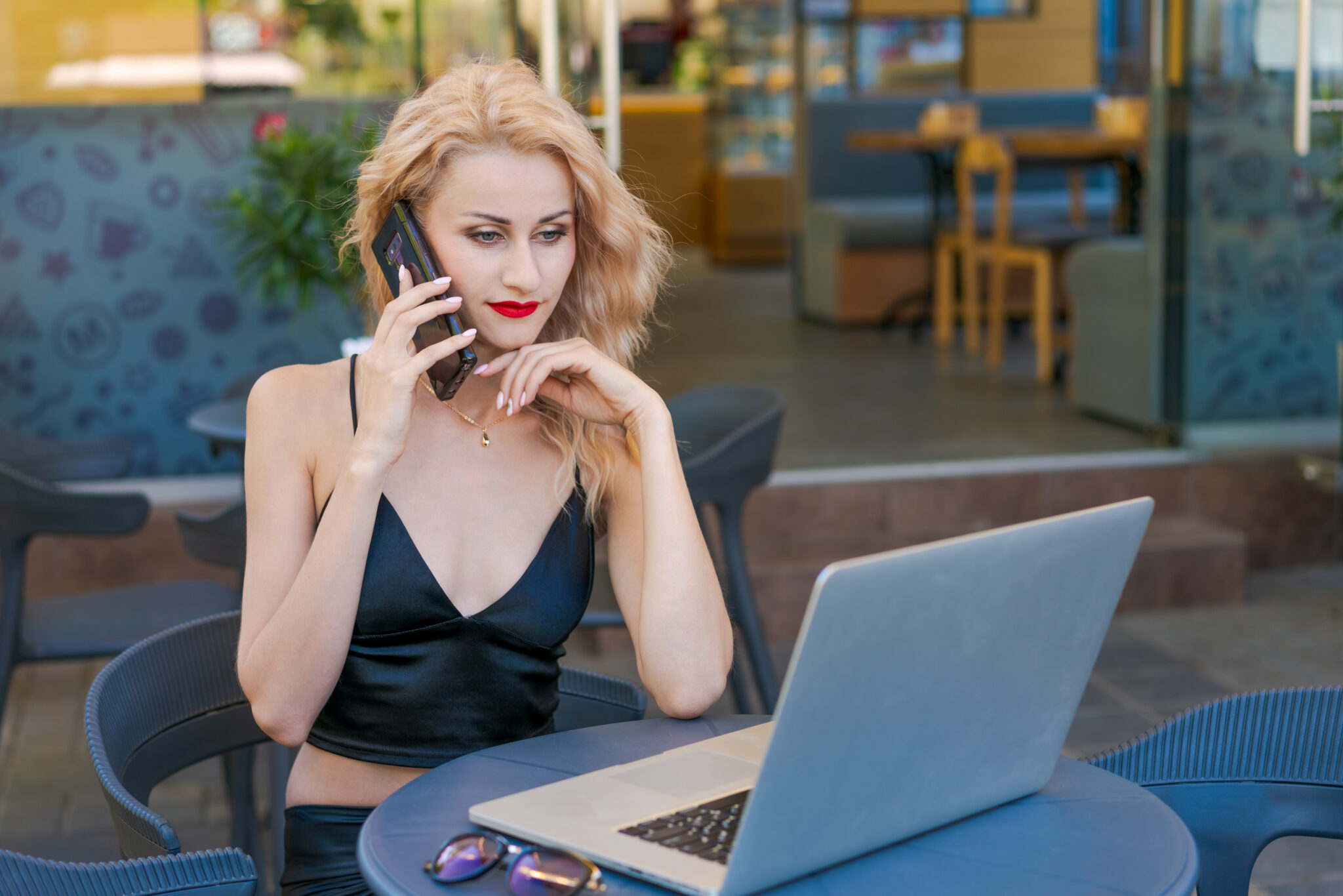 Beautiful woman in glasses sits at table in a street cafe and works on tablet with a laptop. The concept of remote work, free work schedule.