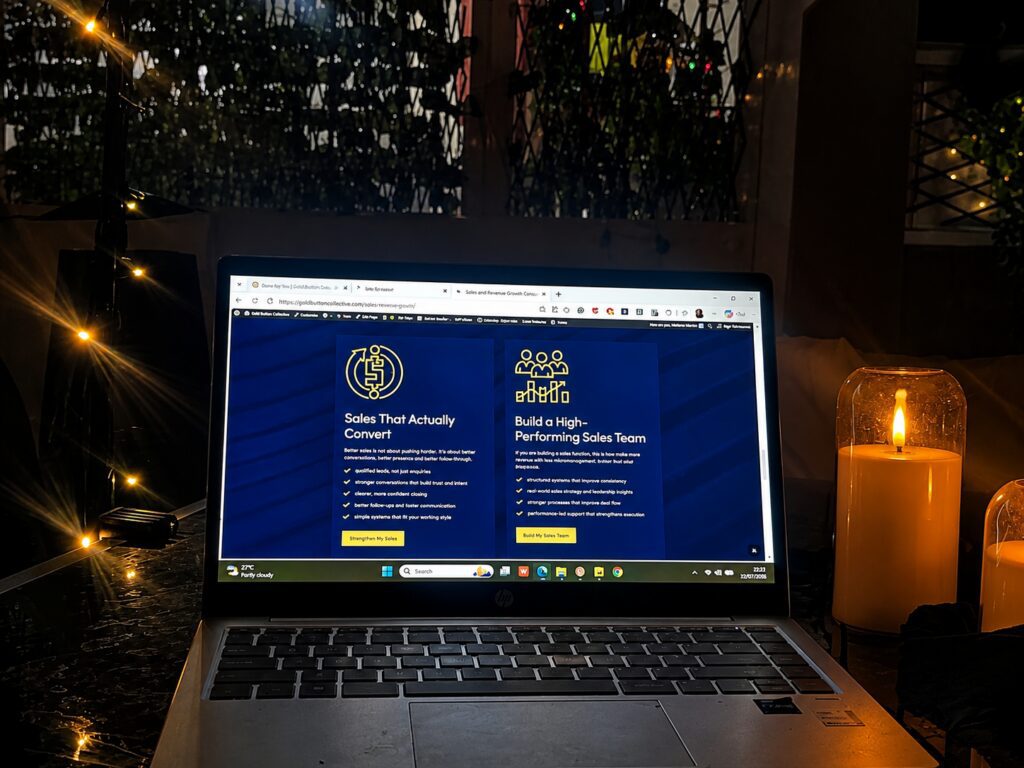 Laptop displaying the Gold Button Collective business growth services website during a late-night strategy and website development session with candlelight in Alicante.