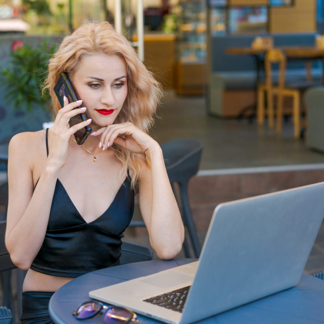 Beautiful woman in glasses sits at table in a street cafe and works on tablet with a laptop. The concept of remote work, free work schedule.